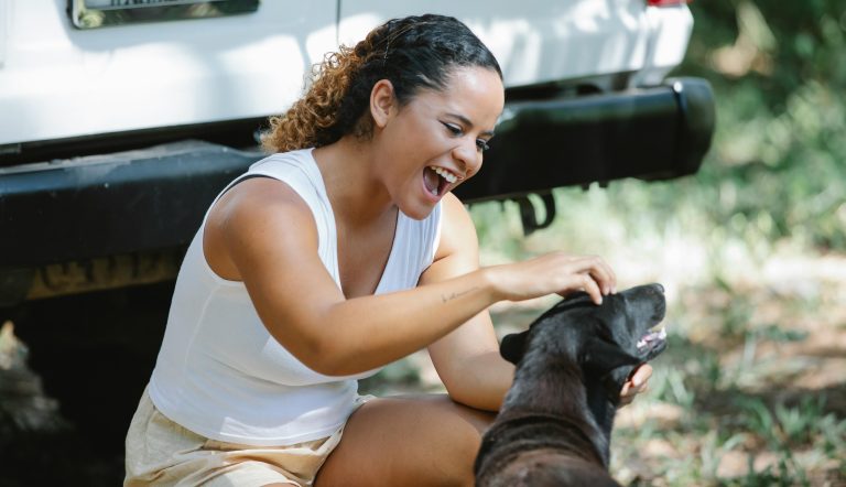 Woman patting her dog next to car