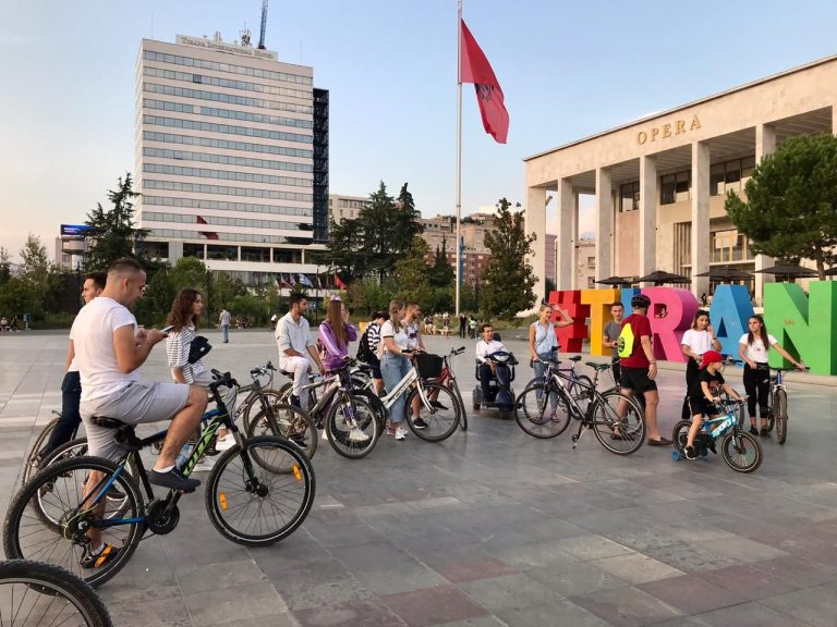 A group of people with bicycles gathered in a public square near large colorful letters spelling "TIRANA."