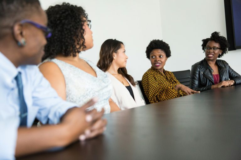 A group of five people, four women and one man, sitting at a table having a discussion.